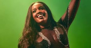 Foto de Iza sorrindo para o público. Ela tem pele negra, cabelos pretos e sorriso no rosto.