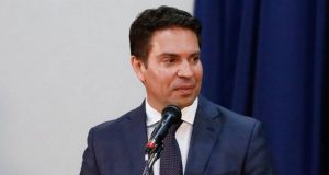 Foto de Ramagem com olhar sério, falando ao microfone e olhando para o lado esquerdo. Ele usa terno azul-marinho.