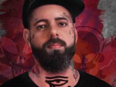 Foto de Tico Santa Cruz sério com barba, rosto tatuado e boné preto.