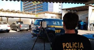 Foto de um funcionário da PF de costas usando uma camisa preta e o nome Polícia Federal em letras amarelas.