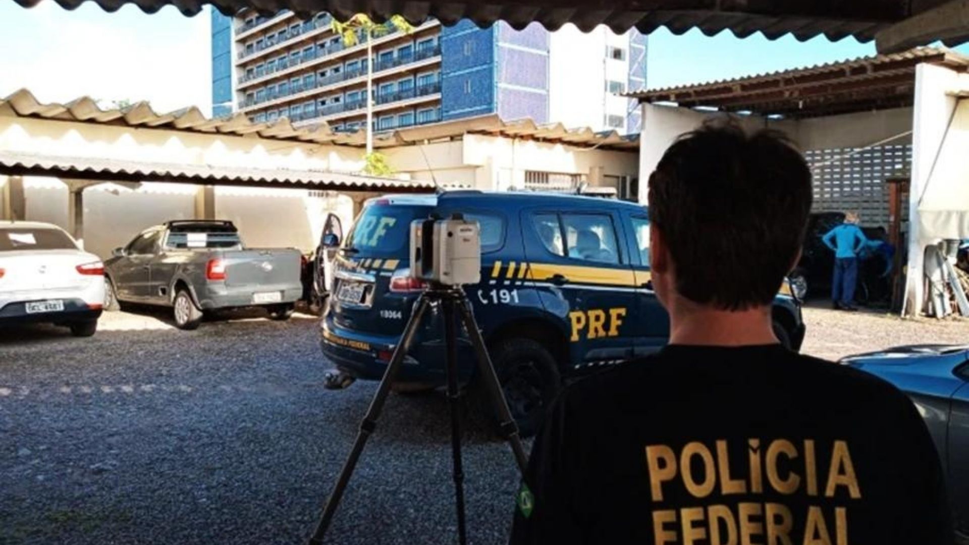 Foto de um funcionário da PF de costas usando uma camisa preta e o nome Polícia Federal em letras amarelas.