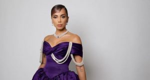 Foto de Anitta com vestido roxo e penteado com cabelo preso. Ela está com expressão séria.