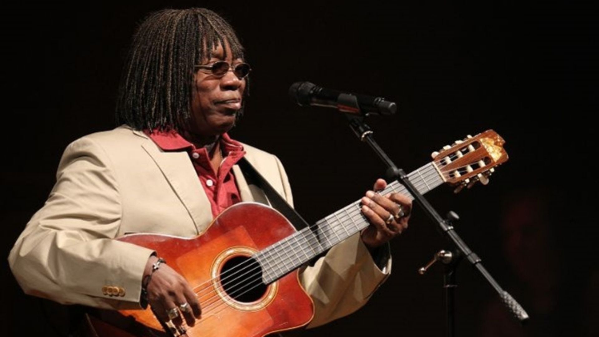 Foto de Milton Nascimento com violão nas mãos, cabelo crespo, pele negra. Ele canta ao microfone.