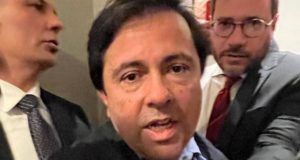 Foto do ex-secretário de Itapevi. Ele tem expressão séria, enquanto é conduzido por dois homens, provavelmente seguranças.