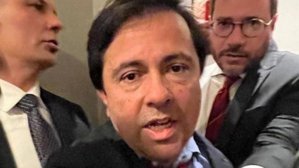 Foto do ex-secretário de Itapevi. Ele tem expressão séria, enquanto é conduzido por dois homens, provavelmente seguranças.