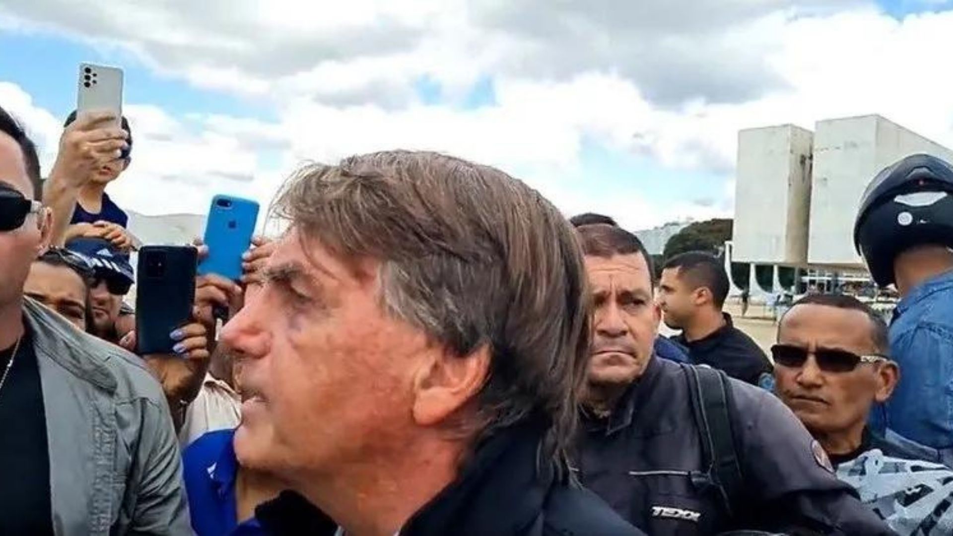 Foto de Bolsonaro falando a apoiadores, ele usa roupa preta, tem cabelo grisalho, pele branca e expressão de intimidação.