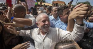Foto de Lula sorrindo com pessoas o segurando na rua. Ele participa de uma manifestação de esquerda.