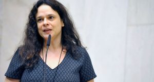 Foto de Janaina Paschoal falando ao microfone. Ela usa uma blusa azul com bolinhas e cabelos pretos longos.