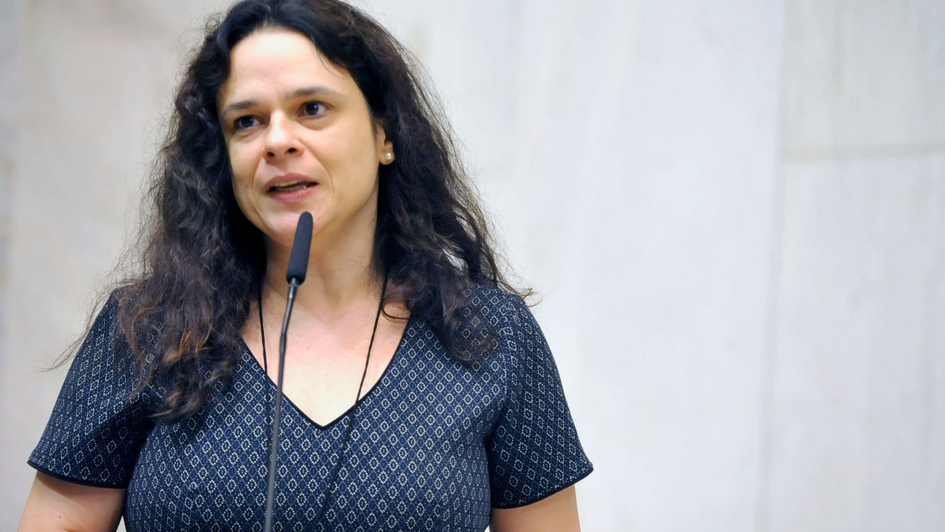 Foto de Janaina Paschoal falando ao microfone. Ela usa uma blusa azul com bolinhas e cabelos pretos longos.