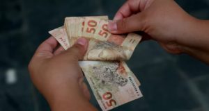 Imagem ilustrativa de uma pessoa manuseando notas de 50 reais.