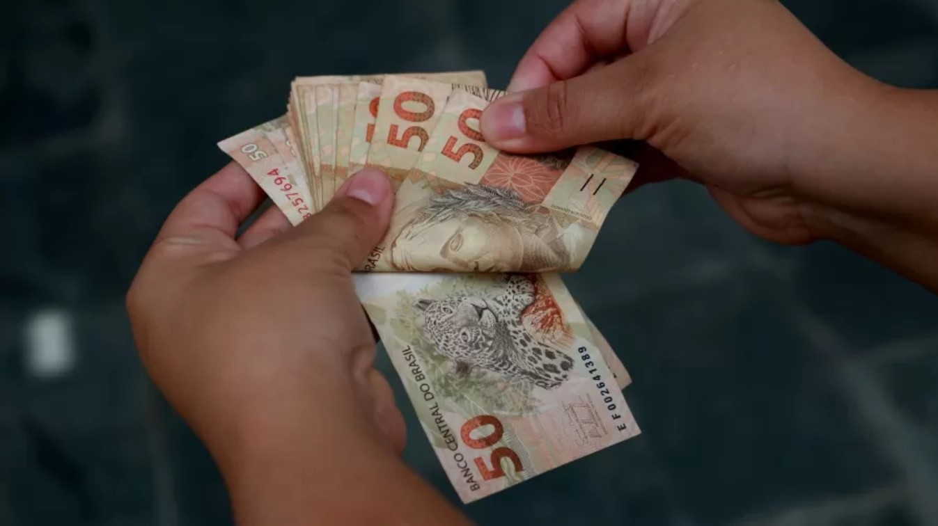 Imagem ilustrativa de uma pessoa manuseando notas de 50 reais.