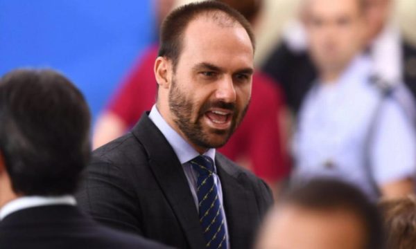 O deputado Eduardo Bolsonaro com a boca aberta. Ele usa terno.