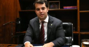 Foto de Antônio Cabral usando um terno preto, gravata vermelha, cabelo preso e pele branca.