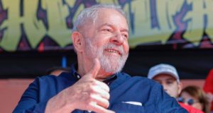 Lula aparece sorrindo em uma foto e fazendo sinal com a mão.