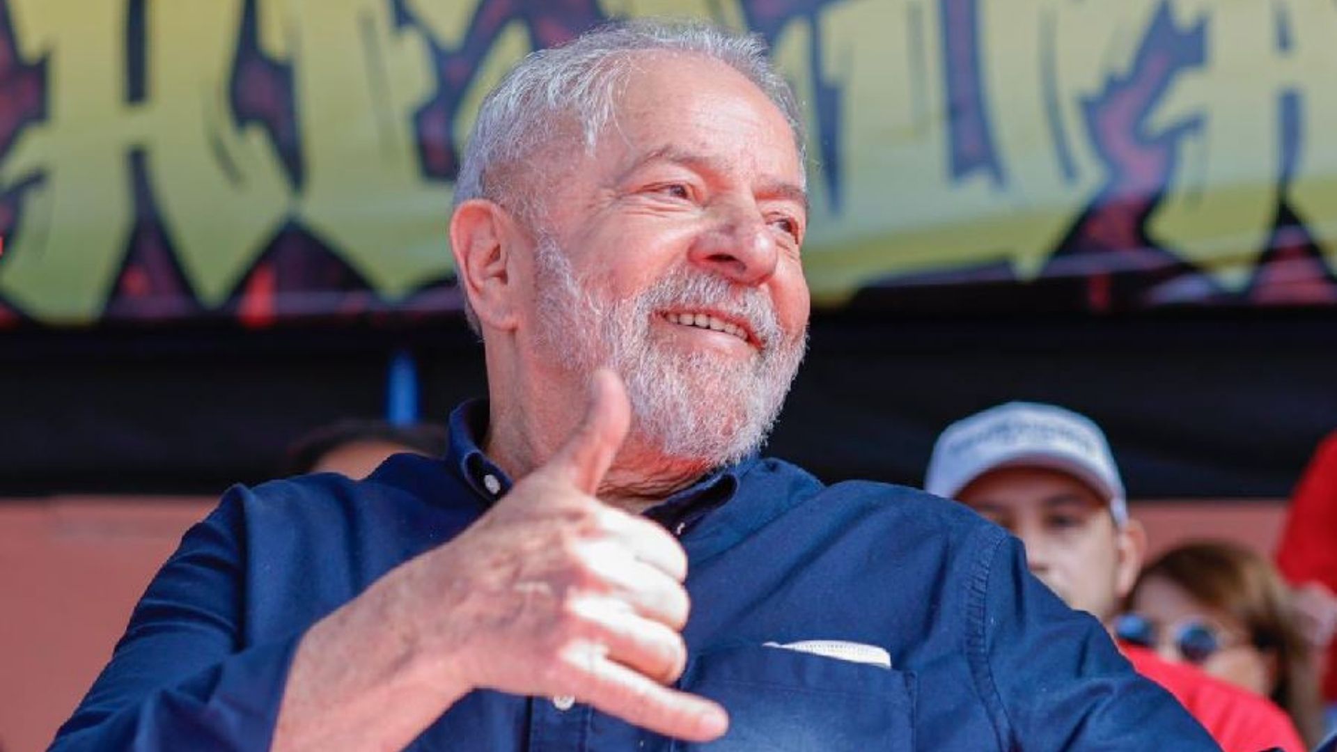 Lula aparece sorrindo em uma foto e fazendo sinal com a mão.