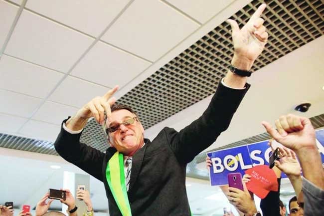 Bolsonaro fazendo gesto de armas com os braços e as mãos