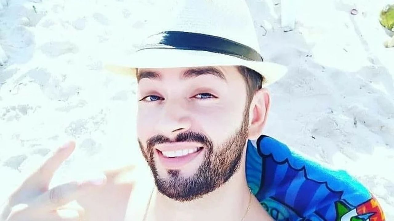 Jorge José da Rocha Guaranho de chapéu de praia, sorrindo e fazendo sinal de paz e amor