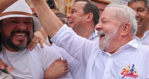 Lula de camisa social branca sorrindo e apertando a mão de populares