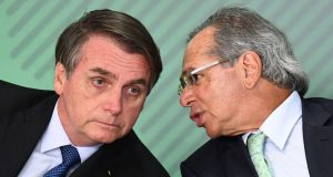 Paulo Guedes falando próximo ao ouvido de Jair Bolsonaro