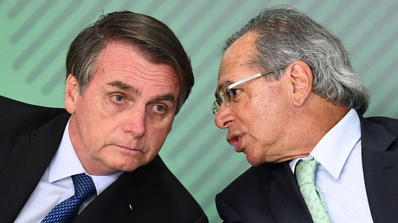 Paulo Guedes falando próximo ao ouvido de Jair Bolsonaro