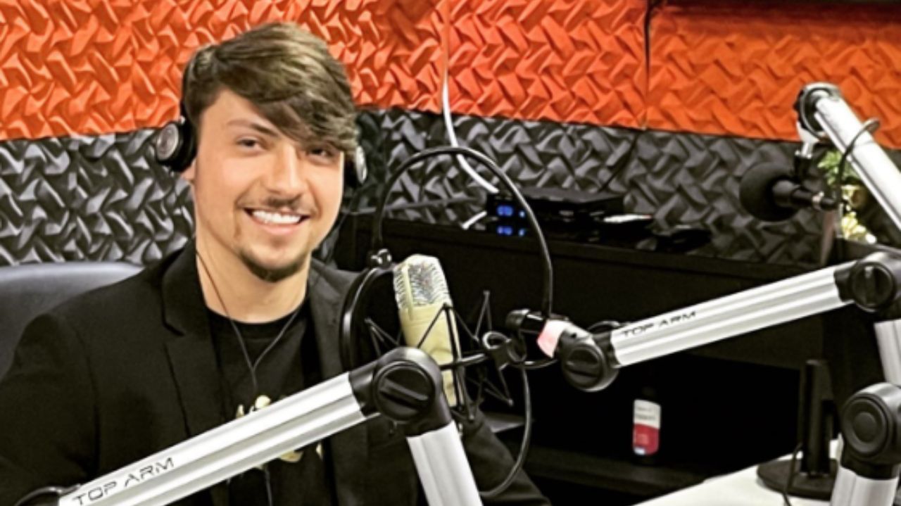 Jair Renan Bolsonaro sorrindo para foto em estúdio de rádio, perto de microfones e usando fones de ouvido