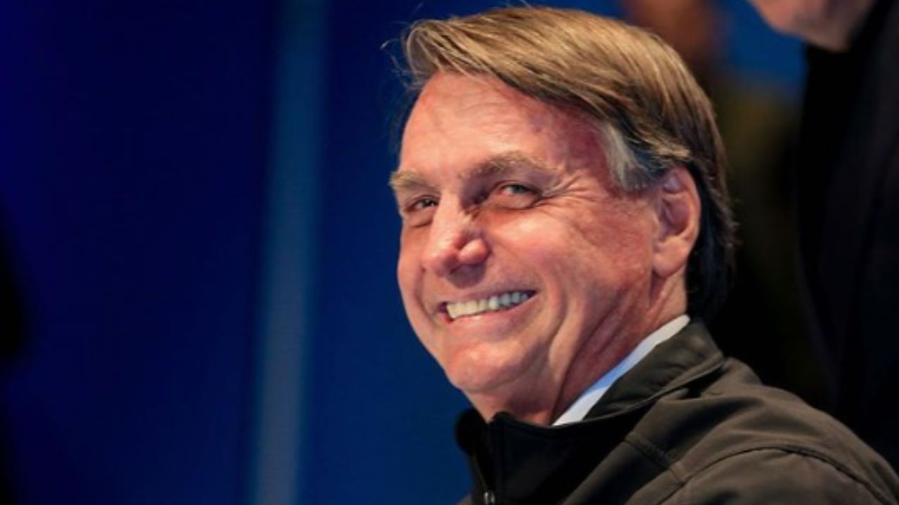 Jair Bolsonaro olhando para o lado e rindo, vestindo casaco preto