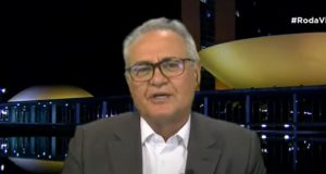 Renan Calheiros falando para a câmera, de óculos, camisa branca e paletó cinza