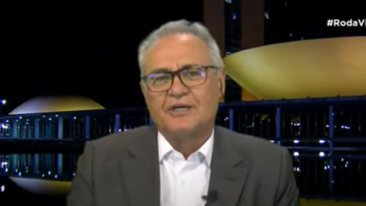 Renan Calheiros falando para a câmera, de óculos, camisa branca e paletó cinza