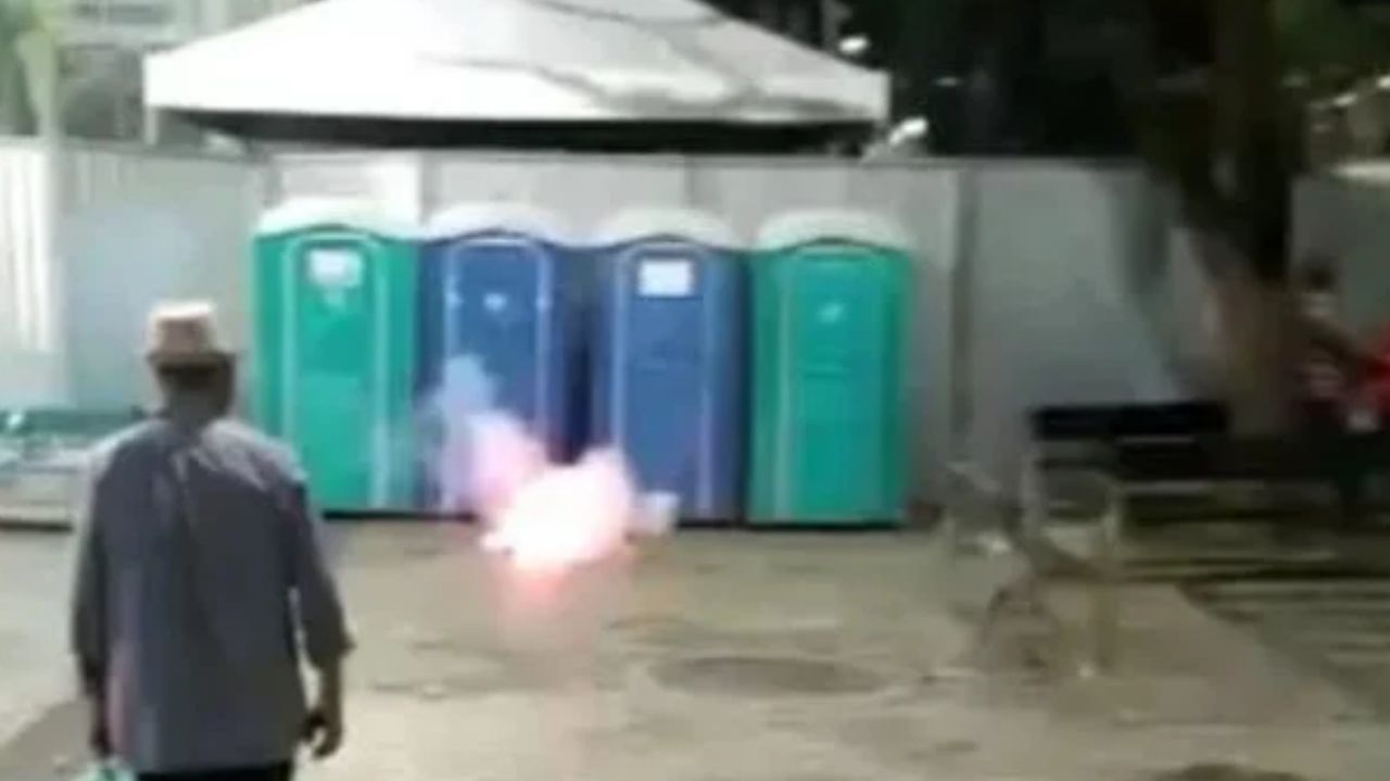 Bomba explodindo perto de banheiros químicos e homem olhando de costas