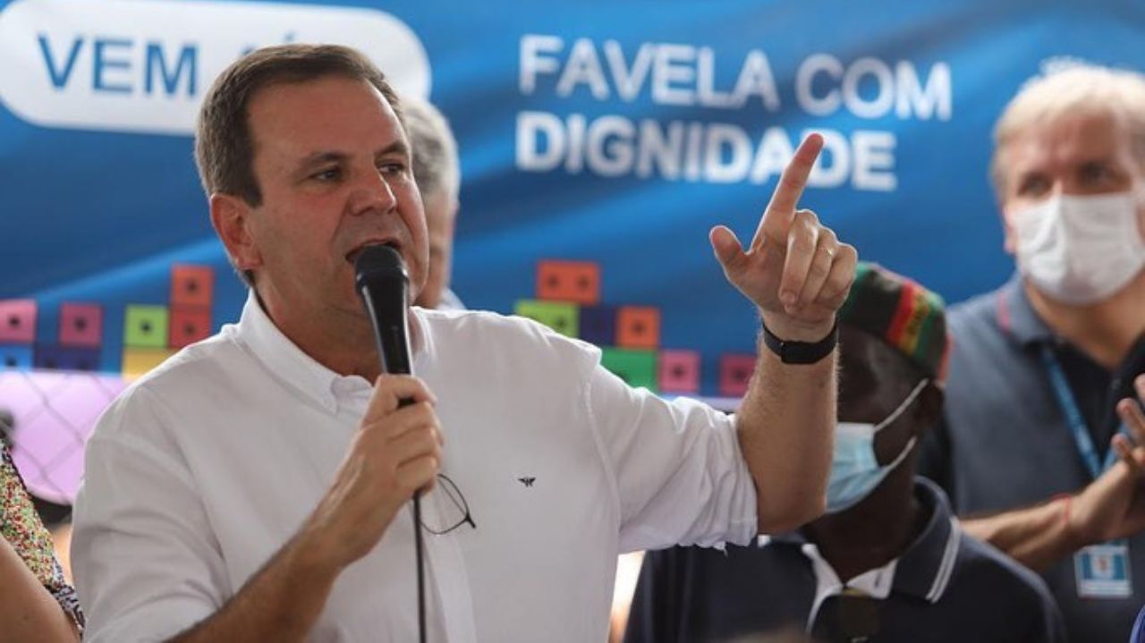 Eduardo Paes de camisa social branca discursando com microfone na mão