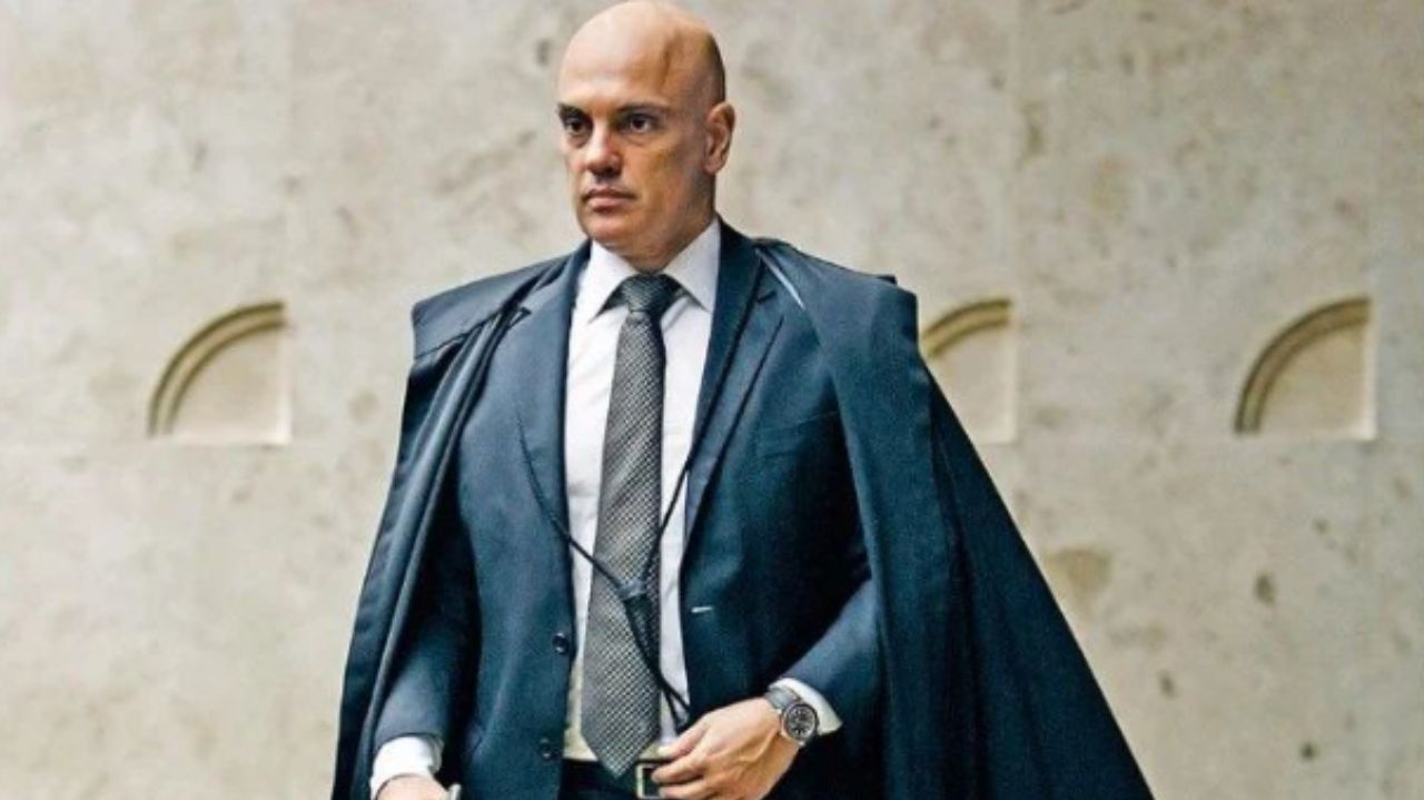 Alexandre de Moraes em pé, vestindo roupa azul marinho e com expressão séria