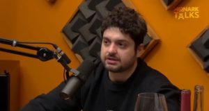 Monark de roupa preta falando em microfone em estúdio de podcast