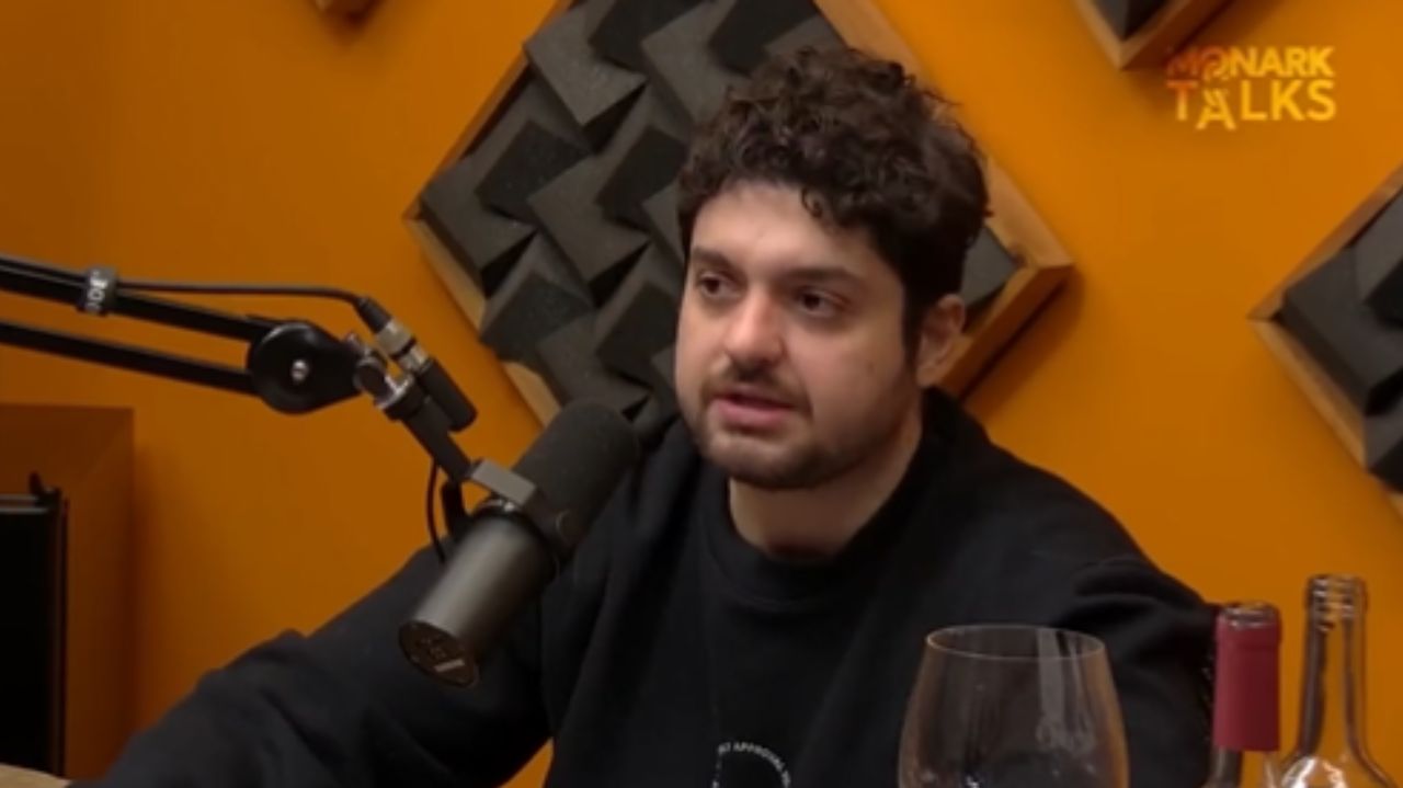 Monark de roupa preta falando em microfone em estúdio de podcast
