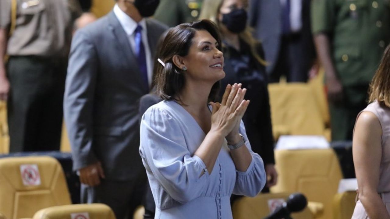 Michelle Bolsonaro com as mãos unidas e sorrindo