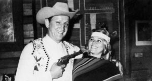 Henning Albert Boilesen em foto em preto e branco sorrindo e com arma apontada para mulher