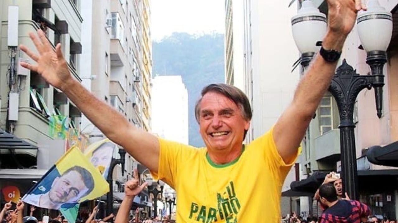 Jair Bolsonaro com camiseta verde e amarela e braços levantados em manifestação