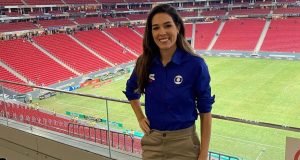 Renata Silveira posando sorrindo e com a mão na cintura, vestindo uniforme da Globo, no estádio Mané Garrincha