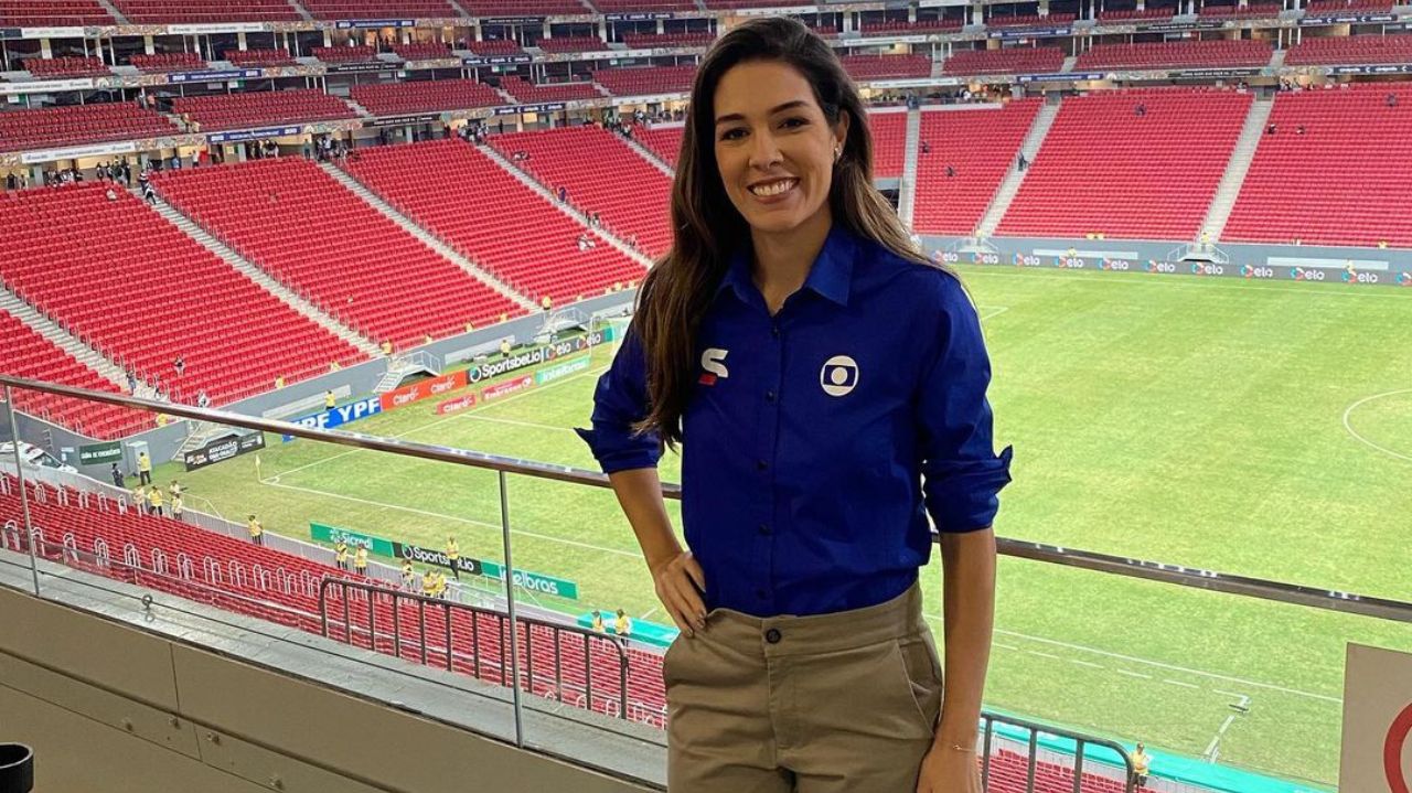 Renata Silveira posando sorrindo e com a mão na cintura, vestindo uniforme da Globo, no estádio Mané Garrincha