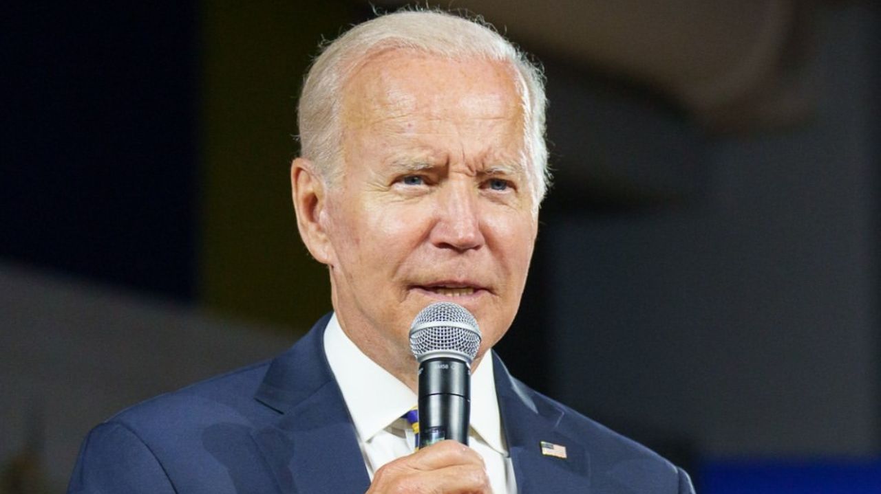 Joe Biden de terno azul marinho e camisa branca, falando em microfone