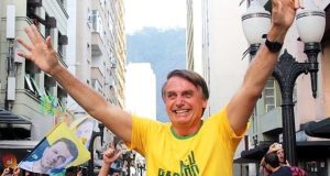 Jair Bolsonaro com camisa verde e amarela e os braços levantados no meio do povo