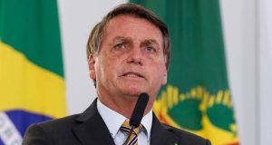 Jair Bolsonaro falando em microfone com bandeiras ao fundo