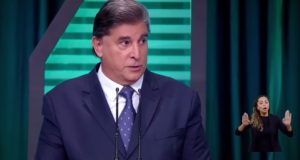 Carlos Nascimento de terno e gravata azuis com expressão séria durante debate