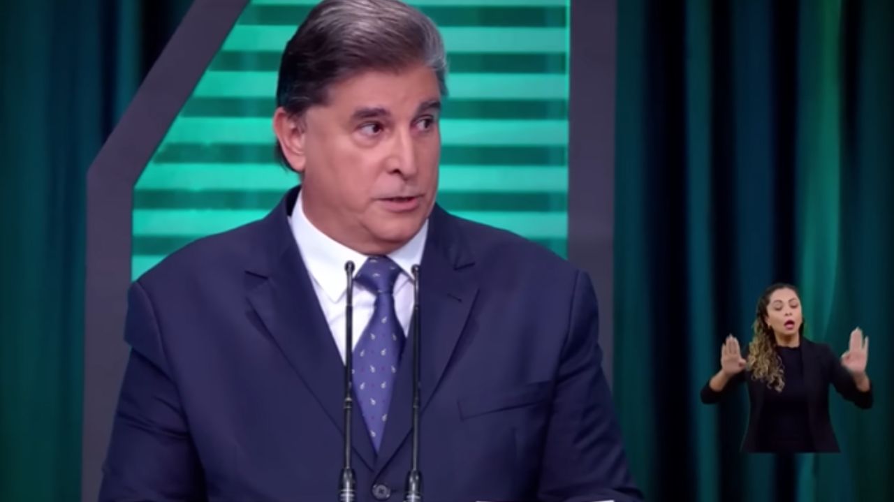 Carlos Nascimento de terno e gravata azuis com expressão séria durante debate