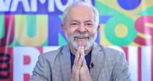 Lula com as mãos unidas e sorrindo em foto