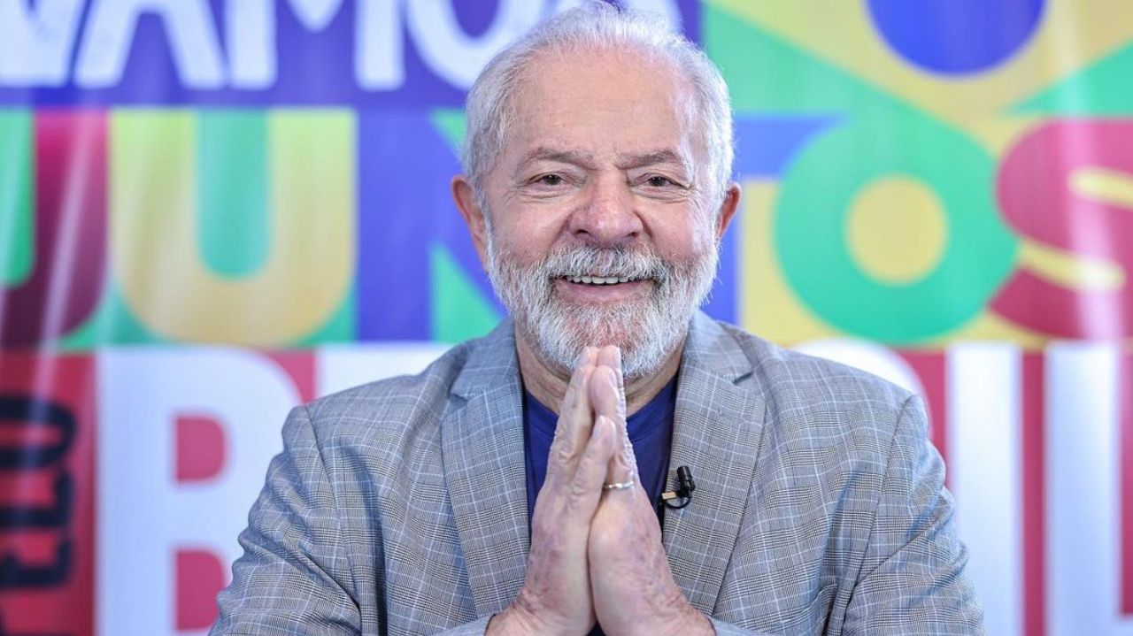 Lula com as mãos unidas e sorrindo em foto