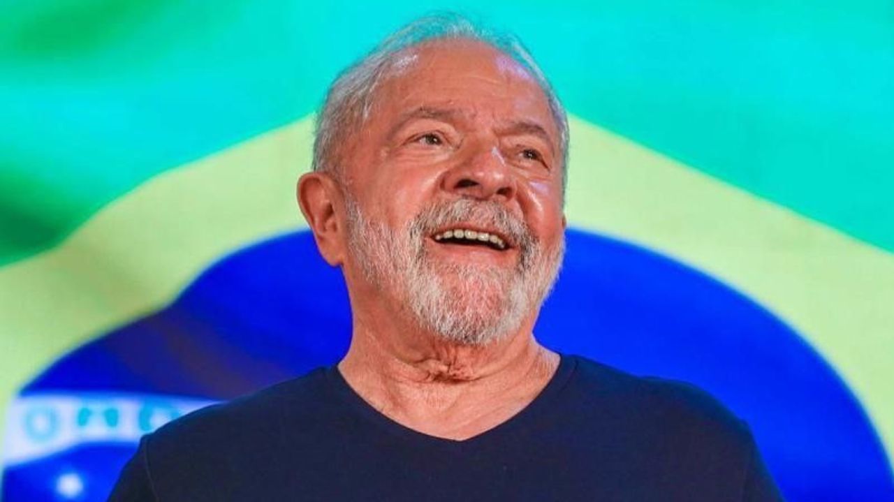 Lula de camiseta azul marinho, sorrindo, com bandeira do Brasil ao fundo