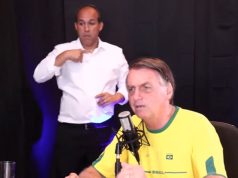 Jair Bolsonaro vestindo blusa do Brasil e falando em microfone com intérprete de libras ao fundo