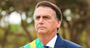 Jair Bolsonaro olhando pra frente de terno e gravata com faixa da Presidência e expressão séria
