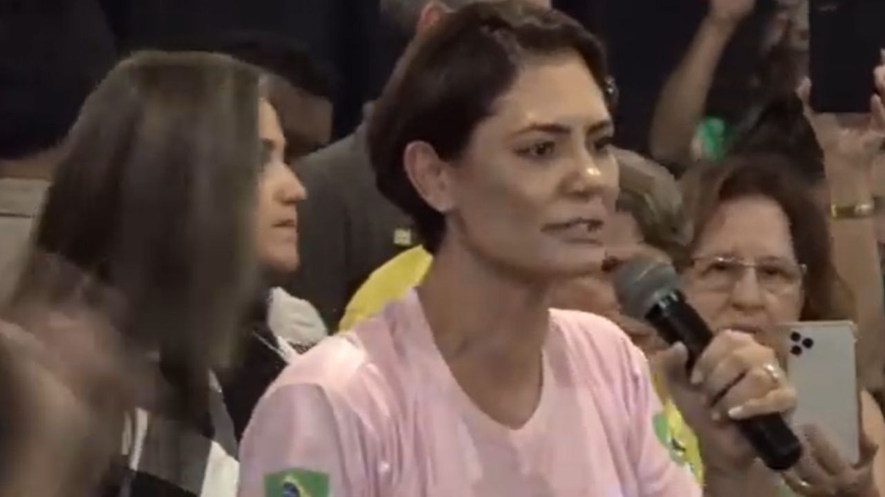 Michelle Bolsonaro de camiseta cor de rosa falando em microfone e de perfil