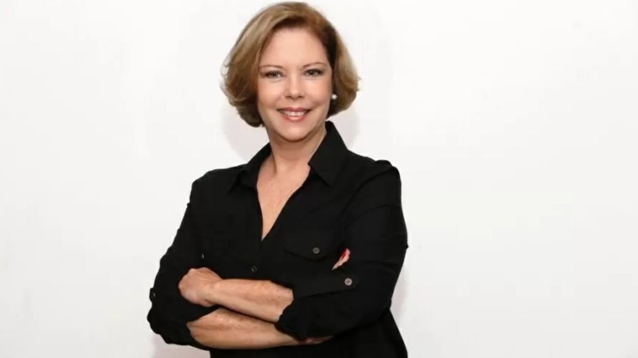Eliane Cantanhêde sorrindo e posando de braços cruzados e roupa preta
